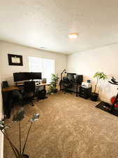 Carpeted home office featuring a textured ceiling