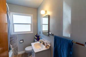 Main floor full bathroom featuring hardwood / wood-style flooring, shower / bathtub combination with curtain, vanity, and toilet