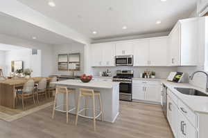 Kitchen with a breakfast bar, sink, white cabinetry, a center island, and appliances with stainless steel finishes