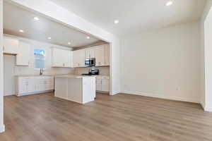 Kitchen with appliances with stainless steel finishes, a center island, white cabinets, and decorative backsplash