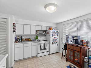 Kitchen with backsplash, white appliances, and white cabinets