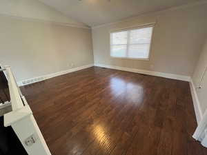 Unfurnished room featuring dark hardwood / wood-style flooring, vaulted ceiling, and ornamental molding