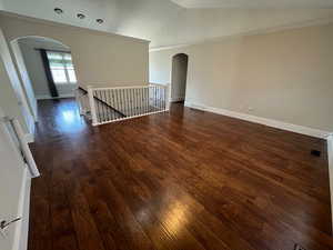 Unfurnished room with dark wood-type flooring, ornamental molding, and vaulted ceiling