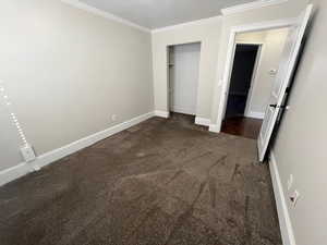 Unfurnished bedroom featuring dark colored carpet, crown molding, and a closet