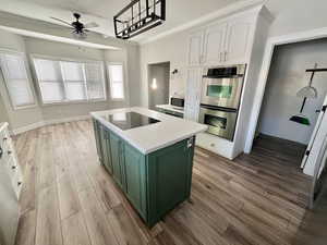 Kitchen with appliances with stainless steel finishes, white cabinets, a center island, green cabinetry, and light hardwood / wood-style flooring