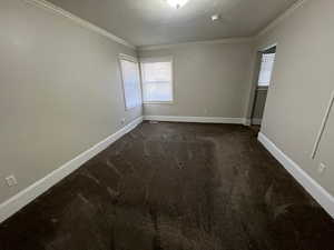 Empty room with ornamental molding and dark colored carpet