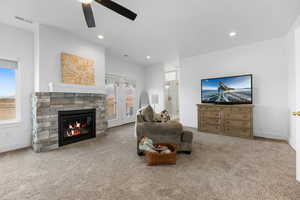 Living room featuring ceiling fan, a stone fireplace, and carpet floors