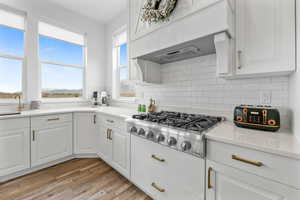 Kitchen featuring sink, hardwood / wood-style flooring, white cabinetry, tasteful backsplash, and stainless steel gas stovetop