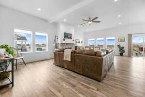 Living room with beam ceiling, ceiling fan, a stone fireplace, and light wood-type flooring