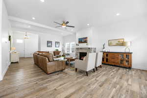 Living room with a stone fireplace, light hardwood / wood-style flooring, beamed ceiling, and ceiling fan with notable chandelier