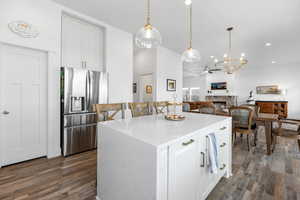 Kitchen featuring pendant lighting, white cabinetry, stainless steel refrigerator with ice dispenser, a fireplace, and a kitchen island