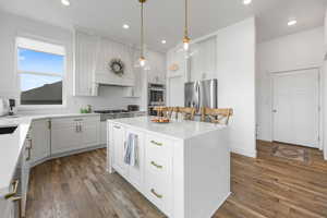 Kitchen with appliances with stainless steel finishes, hanging light fixtures, white cabinets, a kitchen island, and custom exhaust hood