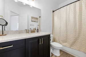 Full bathroom featuring hardwood / wood-style flooring, shower / bathtub combination with curtain, vanity, and toilet