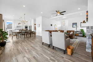 Living room featuring a stone fireplace, ceiling fan with notable chandelier, and light hardwood / wood-style flooring