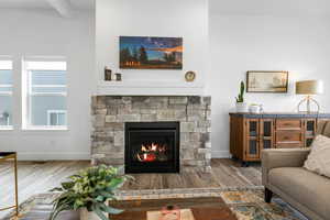 Living room with wood-type flooring, a stone fireplace, and beam ceiling