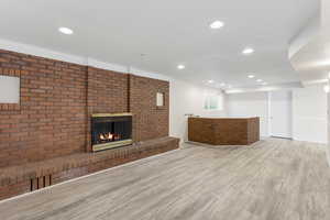 Unfurnished living room featuring brick wall, a fireplace, and light wood-type flooring