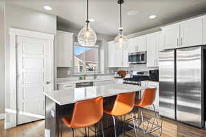 Kitchen with sink, hanging light fixtures, appliances with stainless steel finishes, a kitchen island, and white cabinets