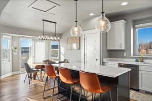 Kitchen with white cabinetry, stainless steel dishwasher, hanging light fixtures, and a kitchen island