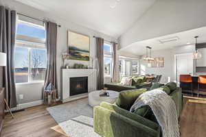 Living room with vaulted ceiling, a healthy amount of sunlight, an inviting chandelier, and light wood-type flooring