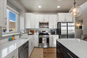 Kitchen with pendant lighting, sink, light hardwood / wood-style flooring, appliances with stainless steel finishes, and white cabinets