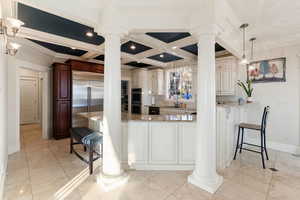 Kitchen with crown molding, hanging light fixtures, coffered ceiling, beamed ceiling, and ornate columns