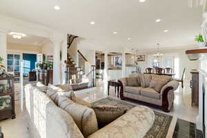 Marble tiled living room with crown molding, an inviting chandelier, and ornate columns