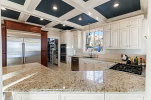 Kitchen featuring coffered ceiling, sink, light granite counters, and stainless steel appliances