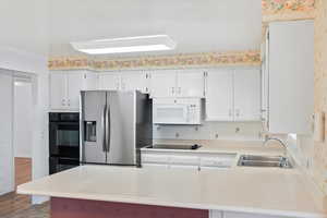 Kitchen featuring sink, white cabinets, backsplash, black double oven, and stainless steel refrigerator with ice dispenser