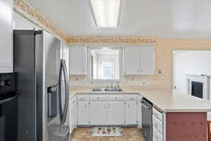 Kitchen with sink, white cabinets, light tile patterned floors, kitchen peninsula, and stainless steel appliances