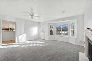 Unfurnished living room with ceiling fan, light carpet, and a textured ceiling