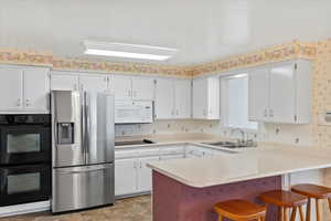 Kitchen with sink, black appliances, kitchen peninsula, and white cabinets