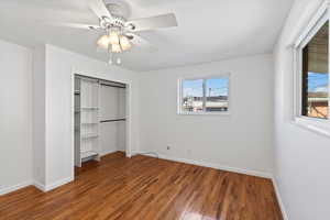 Unfurnished bedroom with multiple windows, ceiling fan, dark hardwood / wood-style flooring, and a closet