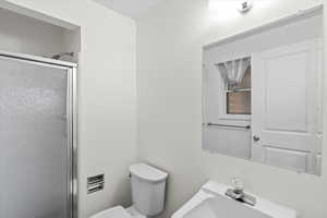 Bathroom with a shower with shower door, sink, and toilet