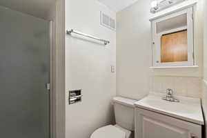 Bathroom with walk in shower, vanity, toilet, and decorative backsplash