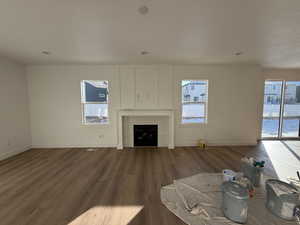 Unfurnished living room with a tiled fireplace, dark wood-type flooring, and a wealth of natural light