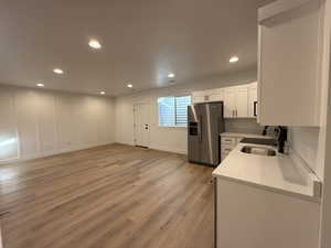 Kitchen featuring sink, light stone counters, white cabinets, high end refrigerator, and light wood-type flooring