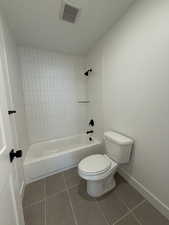 Bathroom featuring tiled shower / bath, toilet, and tile patterned flooring