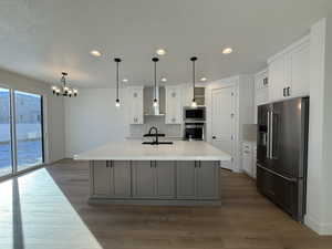 Kitchen featuring wall chimney range hood, a kitchen island with sink, gray cabinetry, stainless steel appliances, and white cabinets