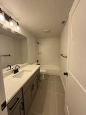 Full bathroom with tile patterned floors, toilet, tiled shower / bath, a textured ceiling, and vanity