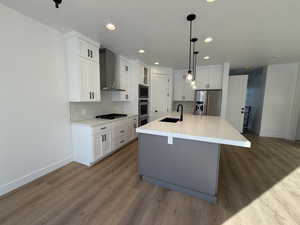 Kitchen featuring built in microwave, stainless steel fridge with ice dispenser, a center island with sink, gas cooktop, and wall chimney range hood