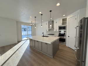 Kitchen with wall chimney range hood, white cabinetry, stainless steel appliances, an island with sink, and decorative light fixtures