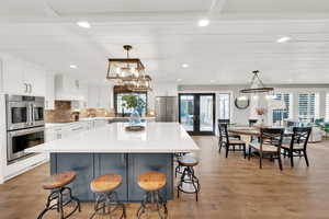 Kitchen featuring appliances with stainless steel finishes, white cabinetry, a kitchen breakfast bar, a center island, and decorative light fixtures