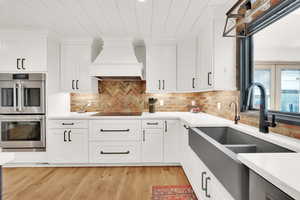 Kitchen featuring custom range hood, stainless steel double oven, and white cabinets