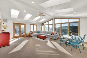 Living room with vaulted ceiling with skylight, light colored carpet, ceiling fan, and french doors