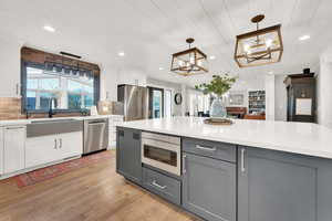 Kitchen featuring gray cabinetry, hanging light fixtures, appliances with stainless steel finishes, light hardwood / wood-style floors, and white cabinets