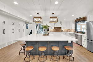 Kitchen featuring a large island, stainless steel appliances, decorative light fixtures, and a kitchen bar