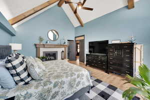 Bedroom with high vaulted ceiling, beamed ceiling, ceiling fan, a brick fireplace, and light hardwood / wood-style flooring