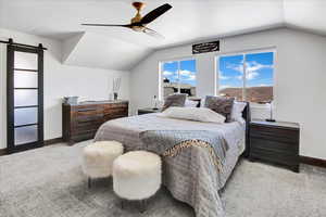 Carpeted bedroom with a barn door, lofted ceiling, and ceiling fan