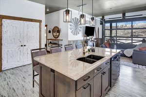 Kitchen featuring a breakfast bar, an island with sink, sink, hanging light fixtures, and light stone countertops