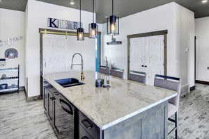 Kitchen with sink, light stone countertops, a center island with sink, decorative light fixtures, and light wood-type flooring